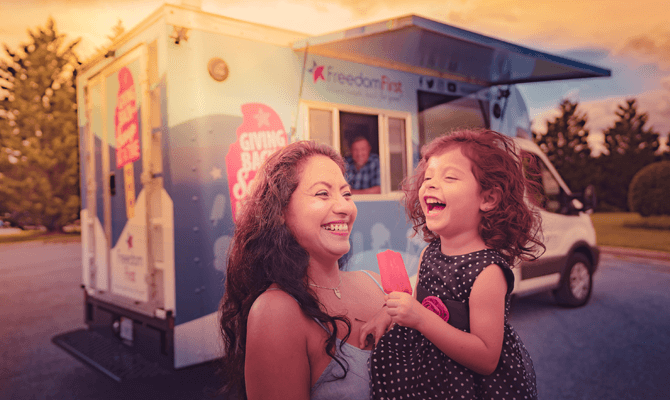 Smiling mother holding her laughing daughter with an ice cream bar in front of Scoop